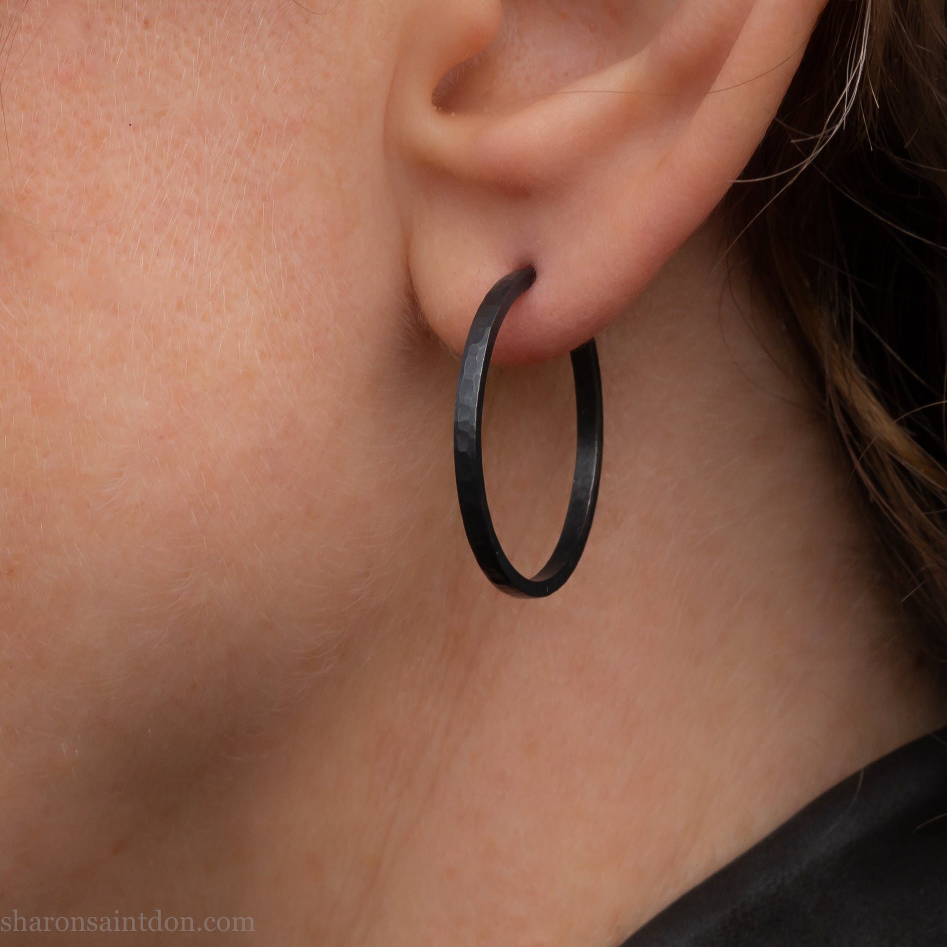 25mm oxidized black sterling silver round hammered hoop earring, close-up on model’s ear.