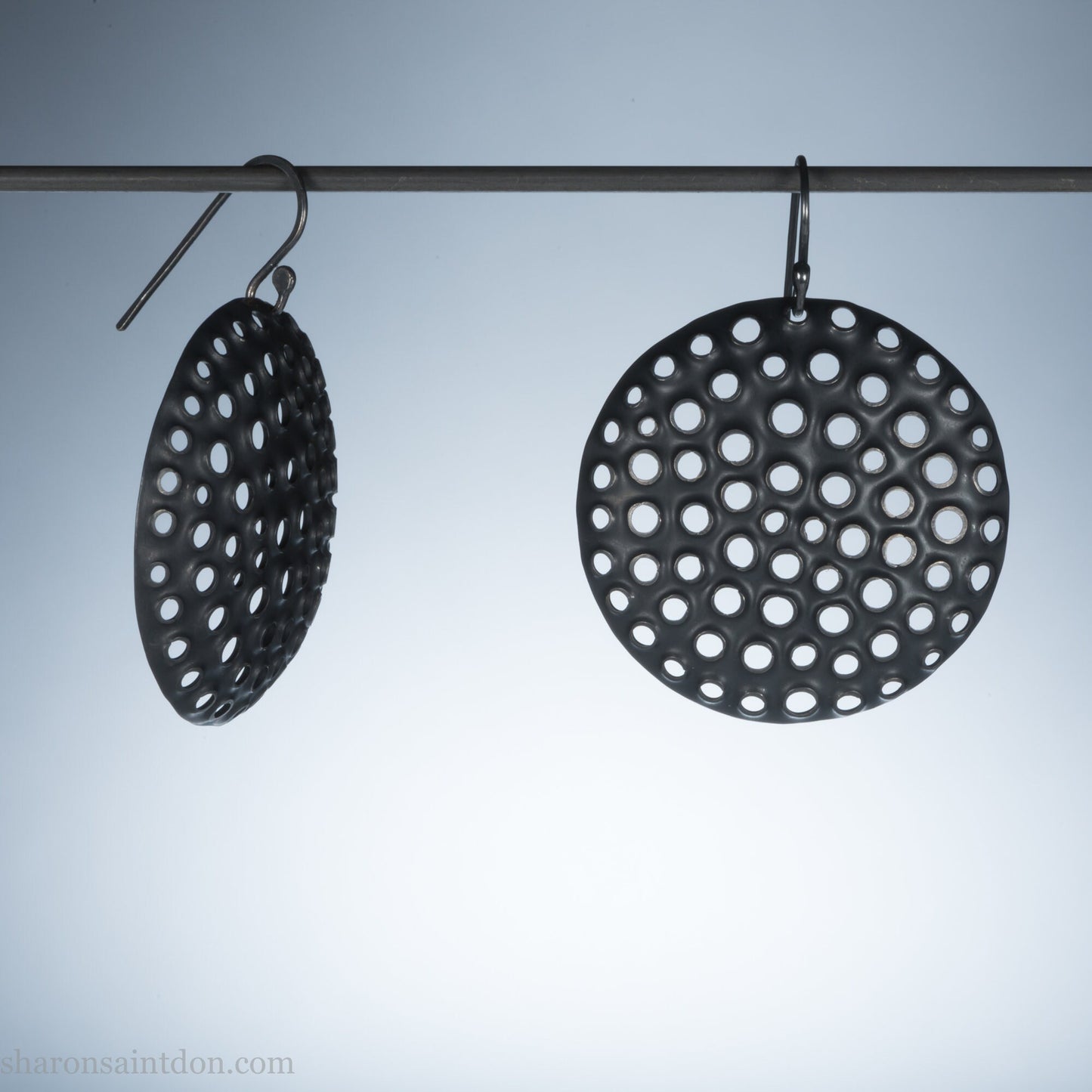 38mm oxidized black sterling silver dangle earrings showing light through perforated disc.
