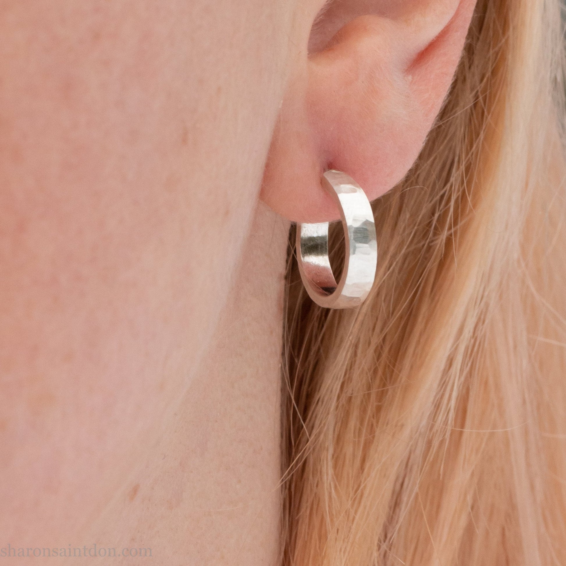 Close up photo of a person's ear wearing a handcrafted 14mm x 3mm hammered solid sterling silver hoop earring.