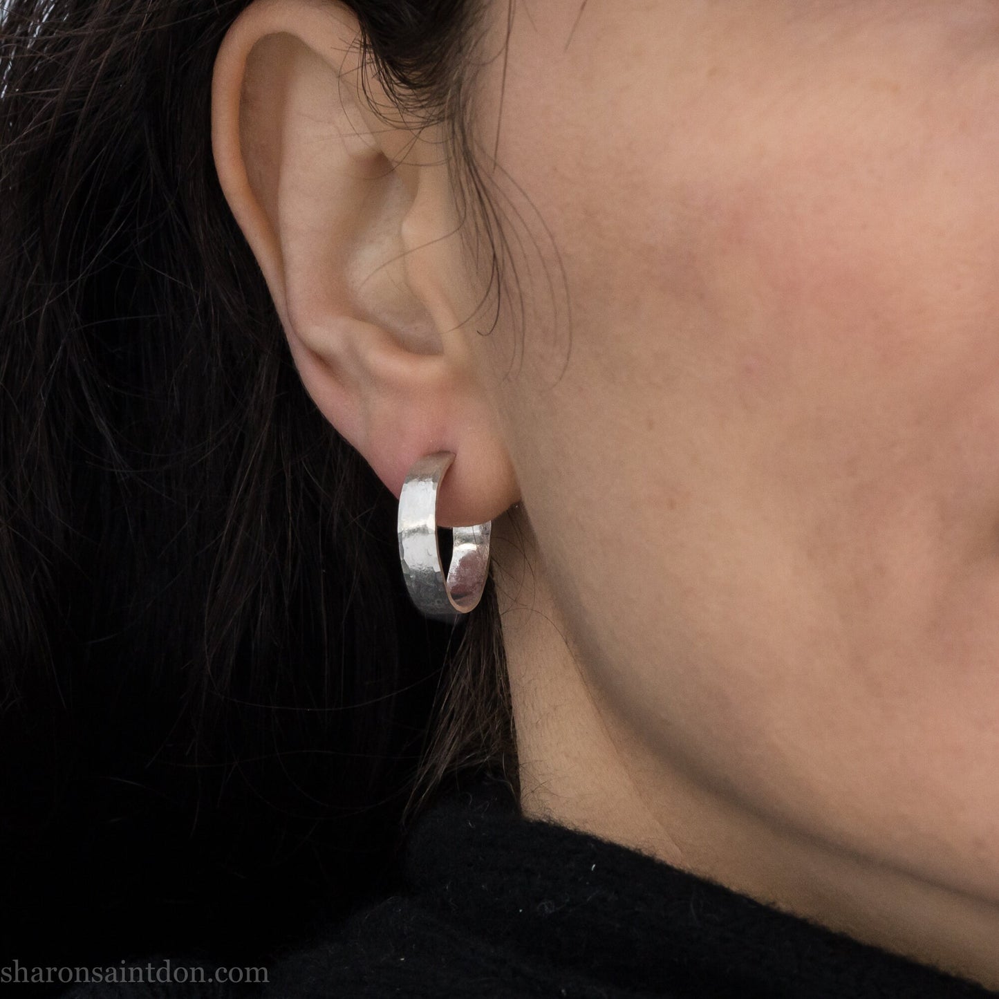 A close-up view of a person wearing handcrafted solid silver hoop earrings, 18mm diameter with a hammered matte finish.