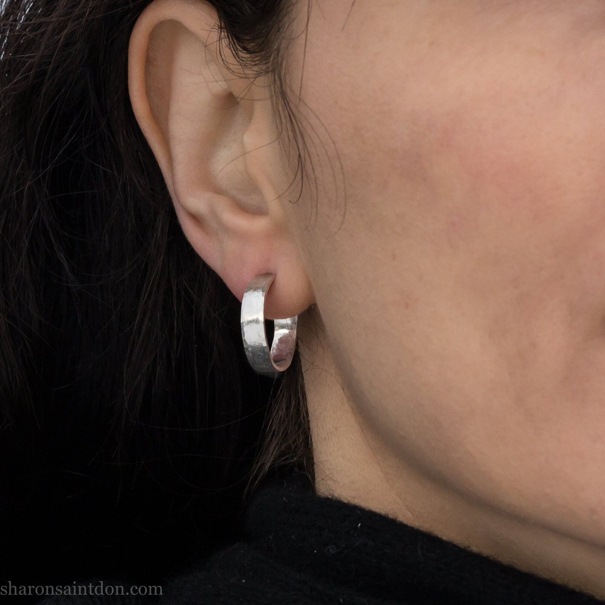 A close-up view of a person wearing handcrafted solid silver hoop earrings, 18mm diameter with a hammered matte finish.