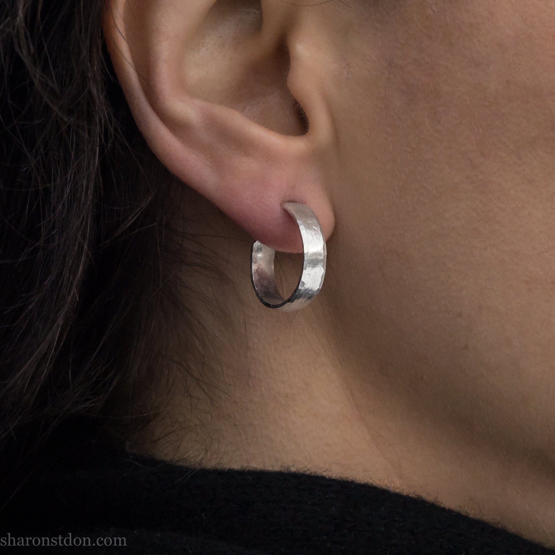 A close-up view of a person wearing handcrafted solid silver hoop earrings, 18mm diameter with a hammered matte finish.